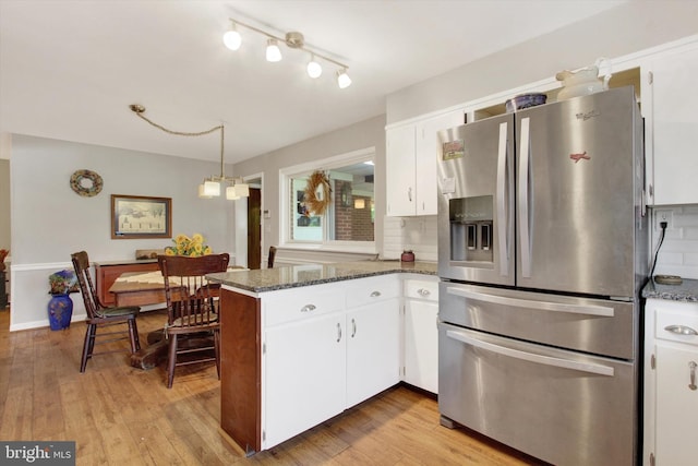 kitchen with stainless steel fridge with ice dispenser, a peninsula, white cabinetry, decorative backsplash, and dark stone counters