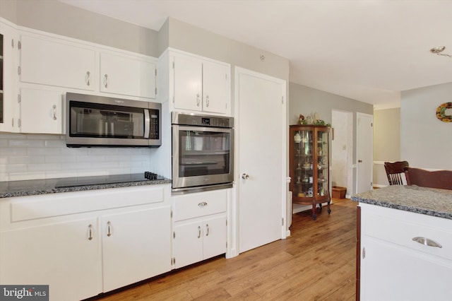 kitchen featuring stainless steel appliances, backsplash, light wood-style flooring, and white cabinetry