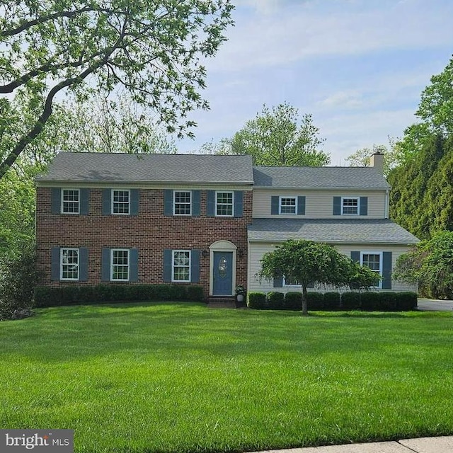 colonial inspired home with a chimney, a front yard, and brick siding