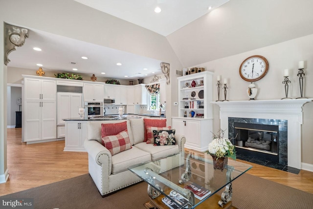 living area with light wood-style flooring, lofted ceiling, a premium fireplace, and recessed lighting