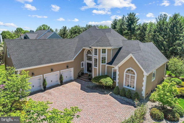 traditional-style home featuring stucco siding, an attached garage, roof with shingles, and decorative driveway