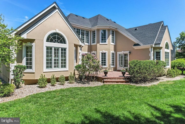 back of house with a lawn, stucco siding, and roof with shingles