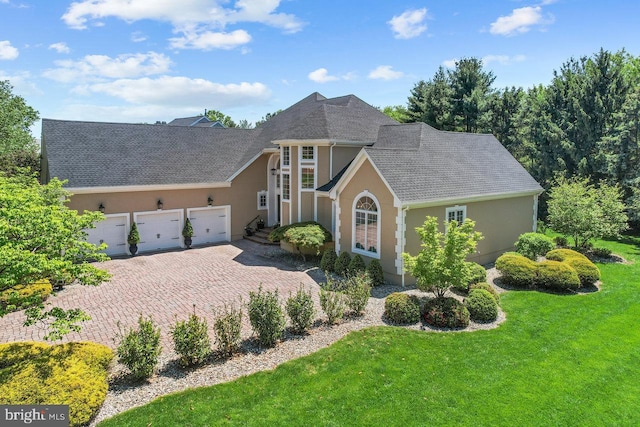 view of front of home featuring stucco siding, a garage, a front yard, driveway, and roof with shingles