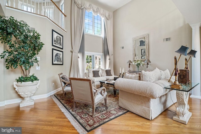 living room featuring a high ceiling, plenty of natural light, light wood finished floors, baseboards, and decorative columns