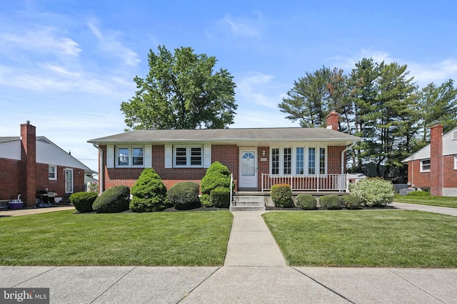 view of front of house featuring brick siding, a porch, a front lawn, and a chimney
