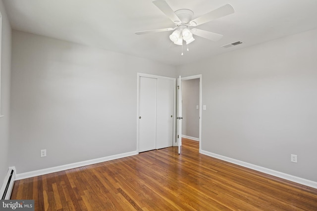 empty room featuring a baseboard radiator, baseboards, wood finished floors, and a ceiling fan