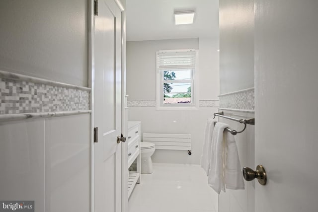 bathroom featuring a wainscoted wall, toilet, and tile walls