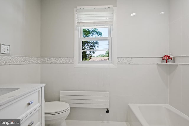 bathroom featuring tile walls, a bath, vanity, toilet, and wainscoting