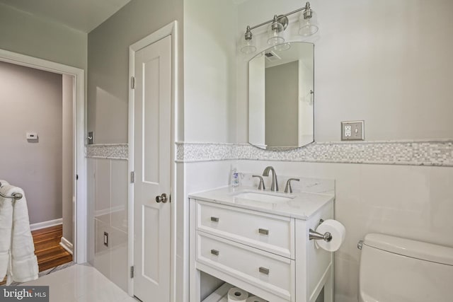 bathroom featuring toilet, a wainscoted wall, vanity, and tile walls