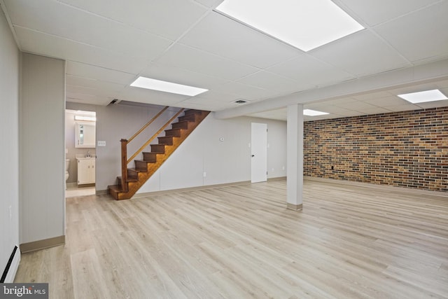 finished below grade area featuring wood finished floors, a paneled ceiling, stairway, brick wall, and baseboards