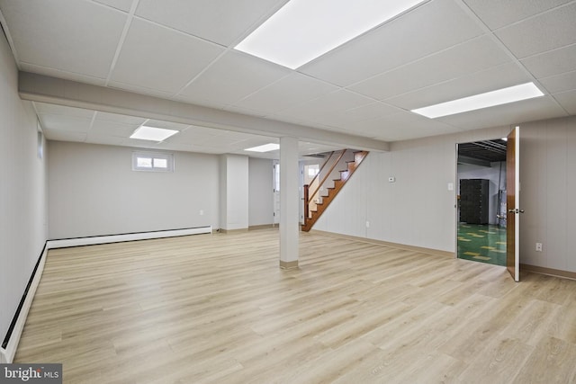 below grade area featuring stairway, wood finished floors, a baseboard radiator, a drop ceiling, and a baseboard heating unit