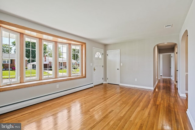 entryway with a baseboard heating unit, arched walkways, wood finished floors, and baseboards