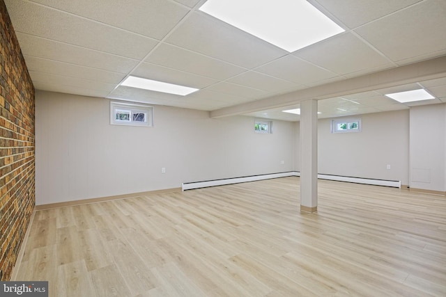 below grade area featuring baseboard heating, light wood-style flooring, a drop ceiling, and baseboards