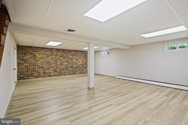 basement featuring a drop ceiling, brick wall, wood finished floors, baseboard heating, and baseboards