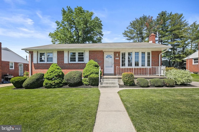 view of front of house featuring a front lawn, brick siding, a chimney, and a porch