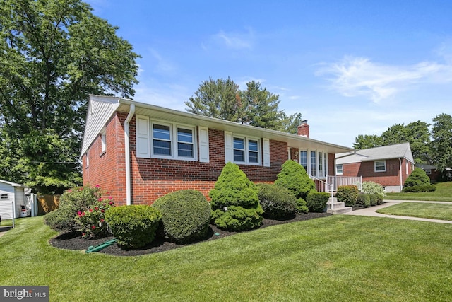 view of front of property featuring brick siding, a chimney, and a front yard