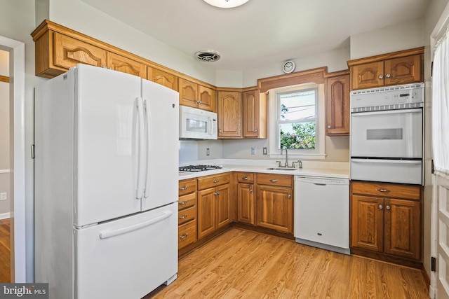 kitchen featuring white appliances, a warming drawer, brown cabinetry, and light wood-style floors