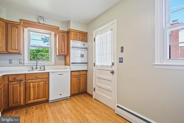 kitchen with white appliances, a warming drawer, a baseboard radiator, a sink, and brown cabinetry