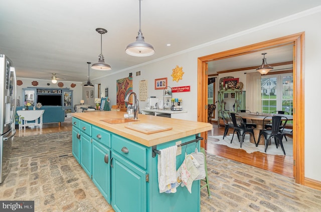 kitchen featuring wood counters, a sink, a kitchen island with sink, ceiling fan, and ornamental molding