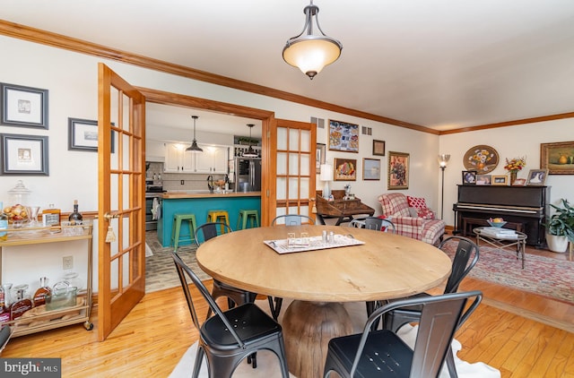 dining room featuring french doors, light wood-style flooring, and ornamental molding