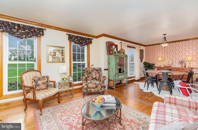 living room featuring plenty of natural light, wood finished floors, ornamental molding, wallpapered walls, and baseboards
