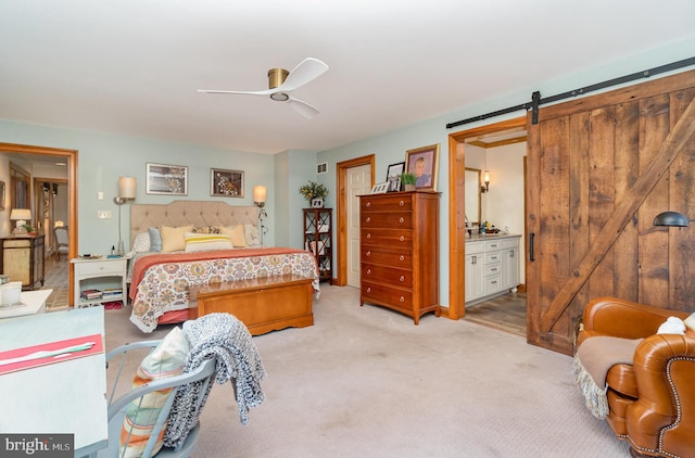 carpeted bedroom with a barn door, ceiling fan, and ensuite bathroom