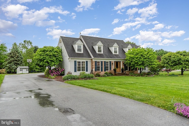 cape cod home featuring a front yard, a storage shed, an outdoor structure, and brick siding