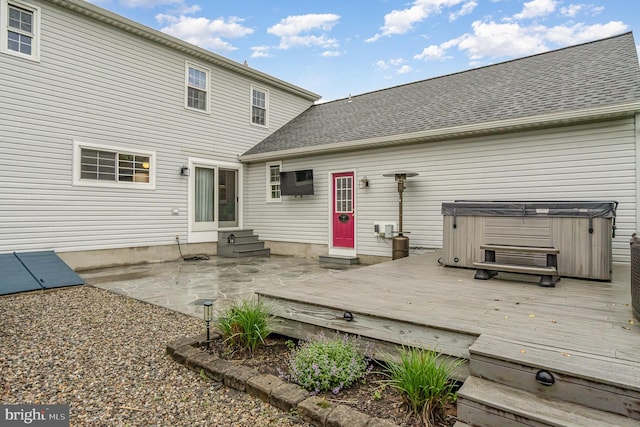 rear view of house featuring a hot tub, a wooden deck, entry steps, roof with shingles, and a patio