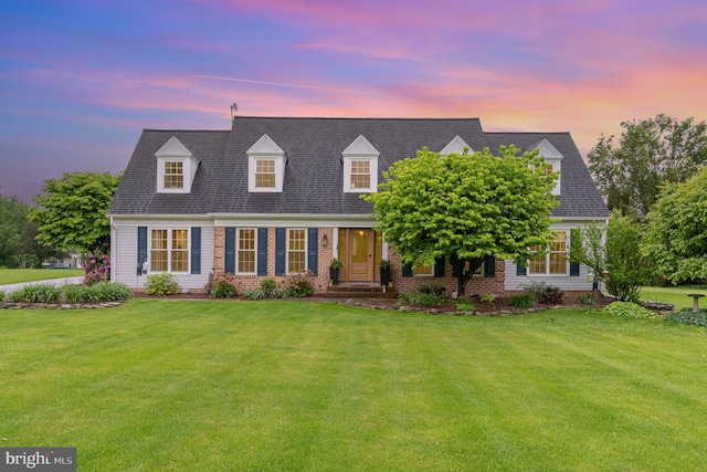 cape cod home with a lawn and brick siding