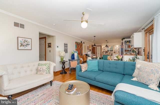 living area featuring light wood-style floors, ceiling fan, ornamental molding, and baseboards