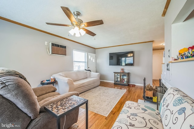 living room featuring a wall unit AC, ceiling fan, wood finished floors, crown molding, and baseboards