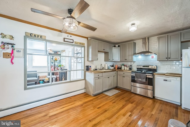 kitchen with white appliances, wall chimney range hood, baseboard heating, gray cabinetry, and a sink