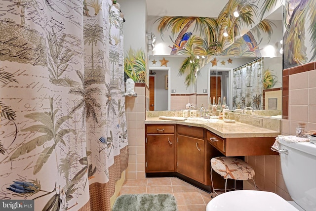 full bathroom featuring tile walls, tile patterned flooring, toilet, vanity, and a wainscoted wall