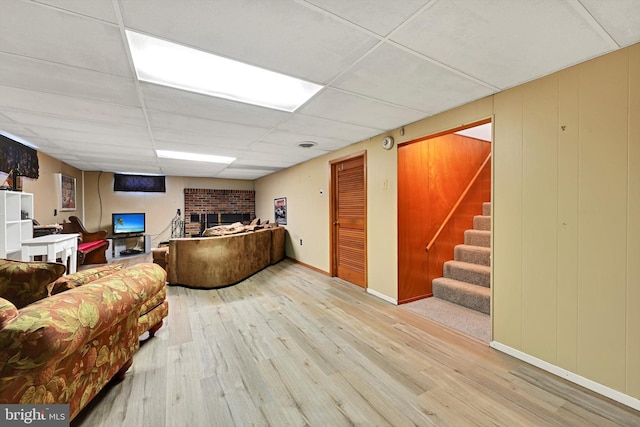 living room with wood finished floors, a drop ceiling, stairway, a fireplace, and baseboards