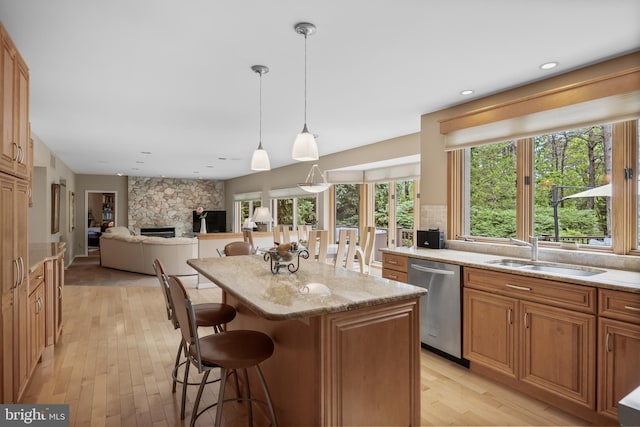 kitchen with stainless steel dishwasher, a breakfast bar, light wood-style floors, a kitchen island, and light stone counters
