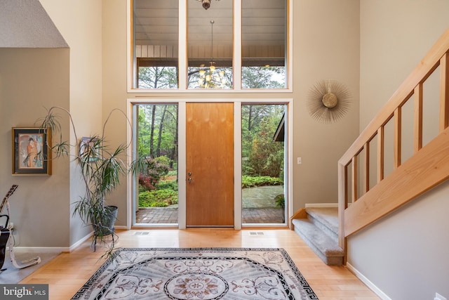 entryway with healthy amount of natural light, a towering ceiling, stairs, wood finished floors, and baseboards