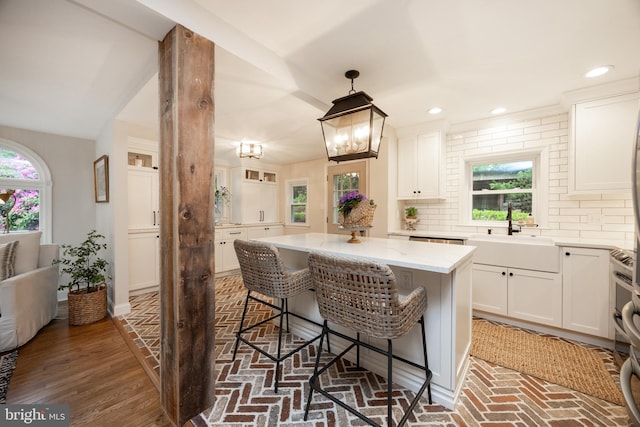 kitchen featuring a sink, a kitchen island, a breakfast bar, white cabinets, and tasteful backsplash