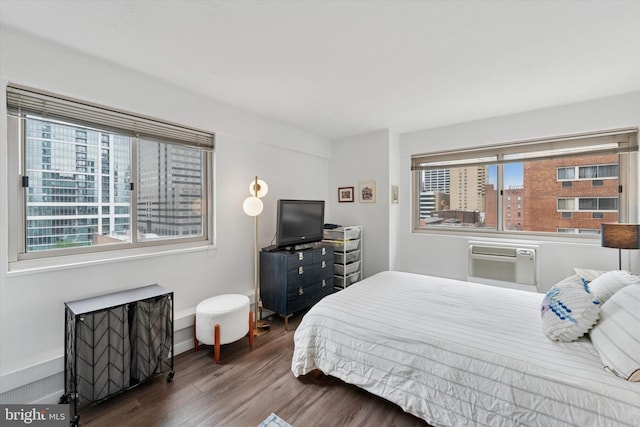 bedroom with a wall mounted air conditioner, wood finished floors, multiple windows, and baseboards