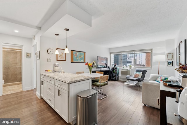kitchen with open floor plan, white cabinetry, wood finished floors, decorative light fixtures, and light stone counters