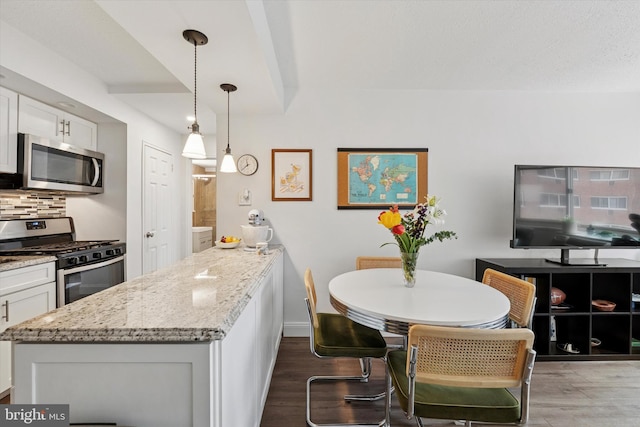kitchen with appliances with stainless steel finishes, wood finished floors, backsplash, light stone counters, and a peninsula