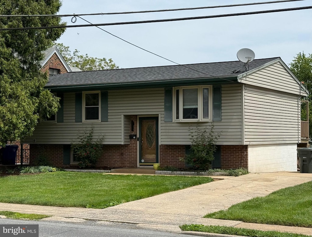 split foyer home with a front yard, brick siding, and roof with shingles