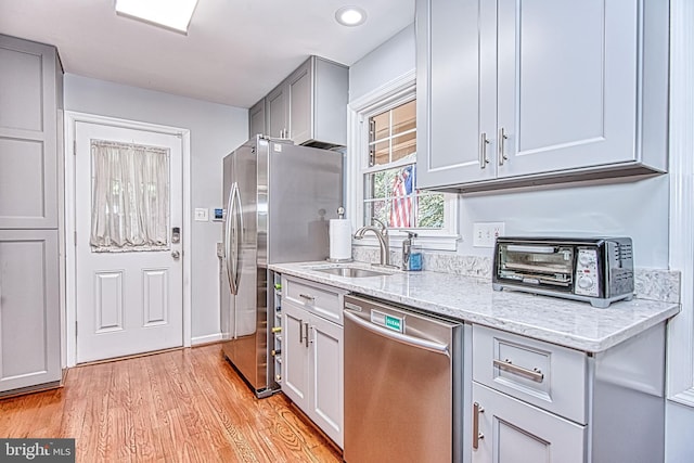 kitchen featuring appliances with stainless steel finishes, a sink, light stone counters, light wood finished floors, and gray cabinets