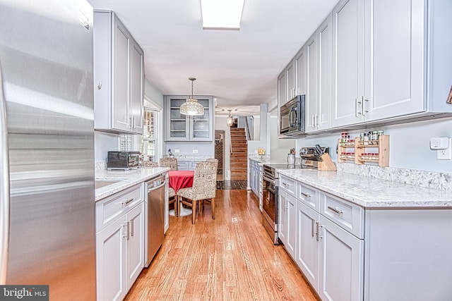 kitchen featuring stainless steel appliances, light wood-style flooring, light stone countertops, pendant lighting, and gray cabinetry