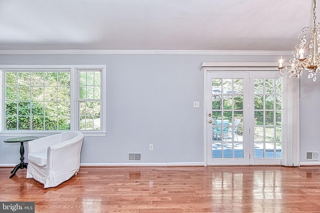 spare room with a chandelier, wood finished floors, crown molding, healthy amount of natural light, and baseboards