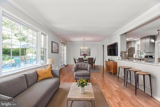 living area with a chandelier, light wood-style floors, and ornamental molding