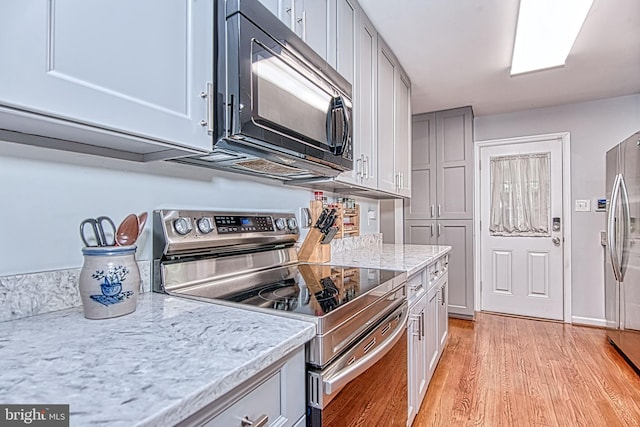 kitchen featuring stainless steel appliances, light wood finished floors, gray cabinetry, and light stone countertops