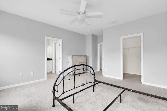 carpeted bedroom featuring a walk in closet, baseboards, ensuite bath, a closet, and ceiling fan