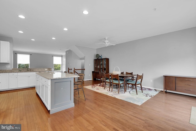 kitchen featuring a kitchen breakfast bar, light wood finished floors, a kitchen island, white cabinets, and ceiling fan