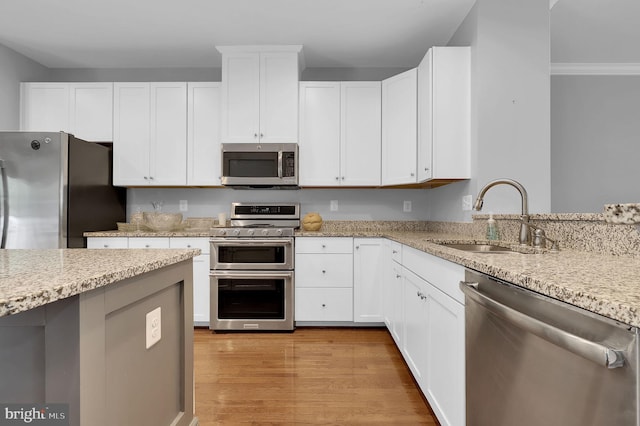 kitchen featuring appliances with stainless steel finishes, a sink, light stone counters, light wood finished floors, and white cabinets