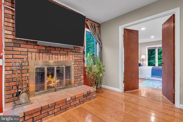 unfurnished living room with wood finished floors, baseboards, a brick fireplace, plenty of natural light, and recessed lighting